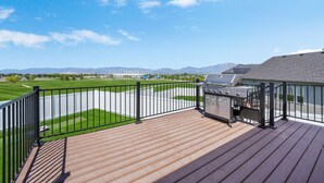 Une terrasse dotée d’un barbecue, offrant une vue sur un terrain de golf et, au loin, sur une chaîne de montagnes.