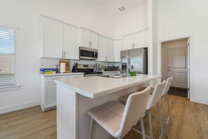 A modern kitchen with white cabinetry, a stainless steel refrigerator, a microwave, and a built-in island with bar stools.