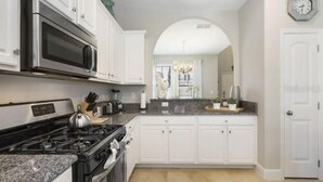 A kitchen with white cabinets, a stainless steel microwave, a gas stove, and a granite countertop. - 6BR Villa Oasis: Private Pool & Spa - Solterra Retreat (Davenport)
