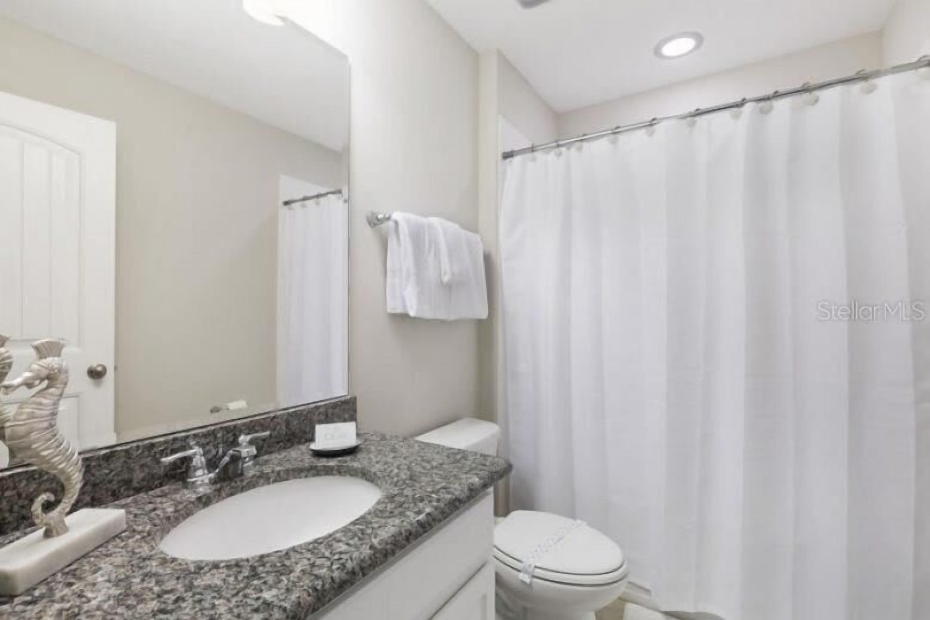 A bathroom with a granite countertop sink, a white toilet, and a shower curtain.