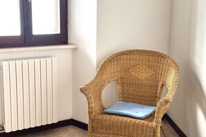 Une pièce d’angle avec un fauteuil en osier, un radiateur et une fenêtre.