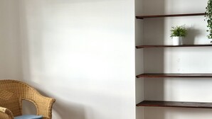 A wicker chair with a blue cushion, a white wall, and a wooden shelf unit with a plant on the top shelf. - S296 - Sirolo, studio flat in the center with sea view (Sirolo)
