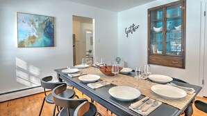 Un comedor con una mesa larga dispuesta para seis personas, un mueble de madera con puertas de cristal y una pared con un cartel que dice 'Gather'.