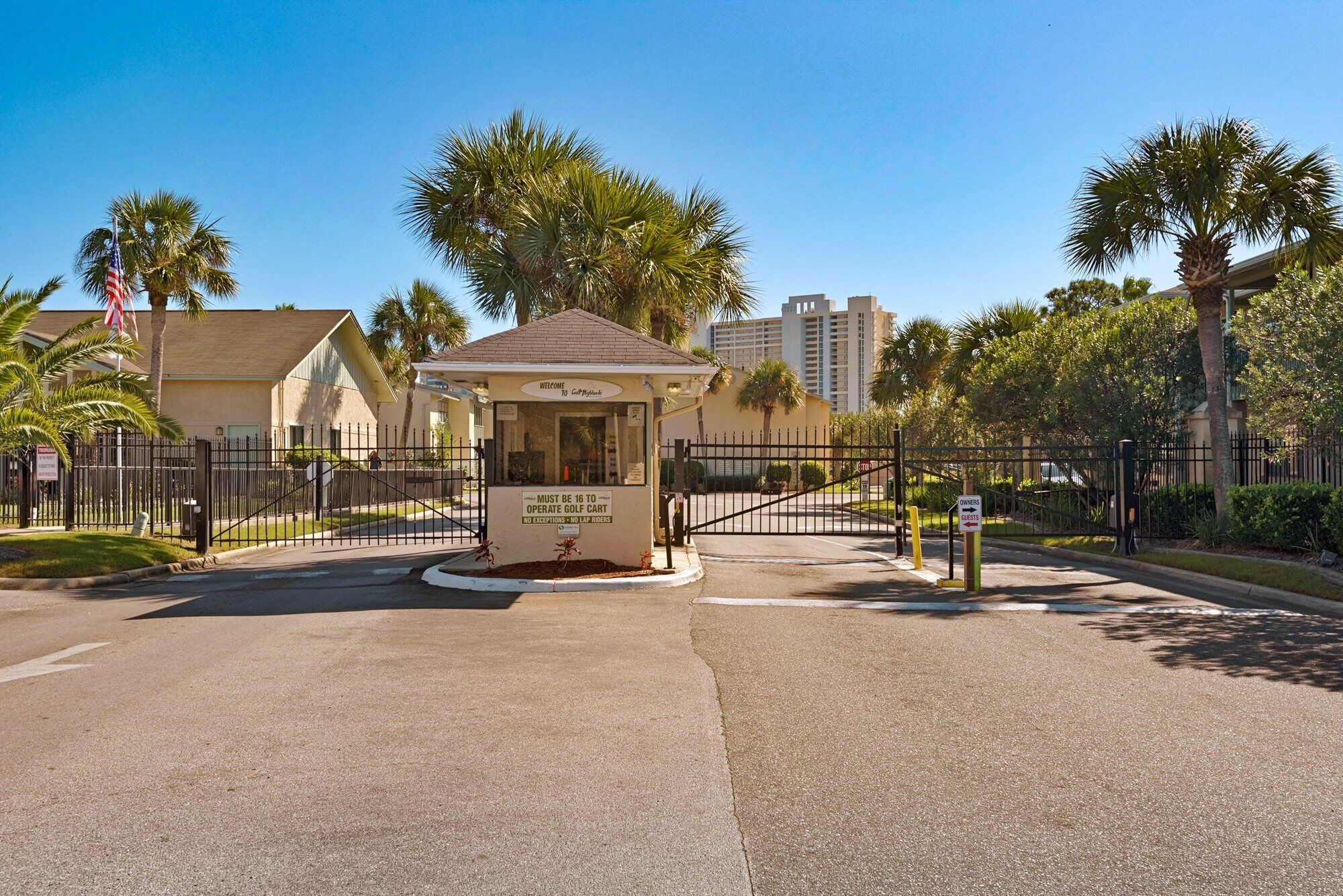 A gated entrance to a golf course with a small kiosk, palm trees, and a clear sky.