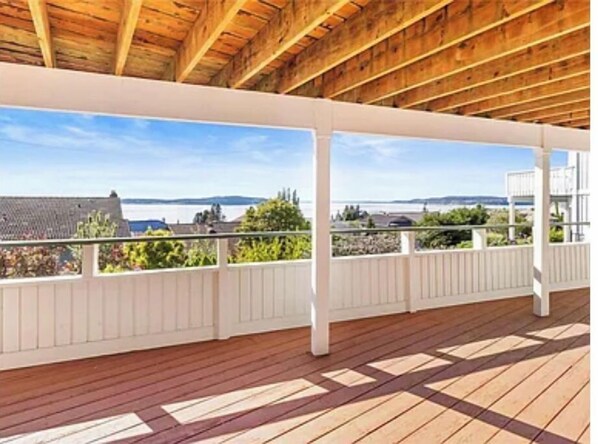 A covered wooden deck with a view of the sea and distant hills.