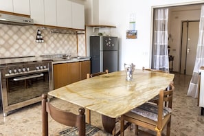 Uma cozinha com mesa de mármore, cadeiras de madeira, geladeira e fogão.