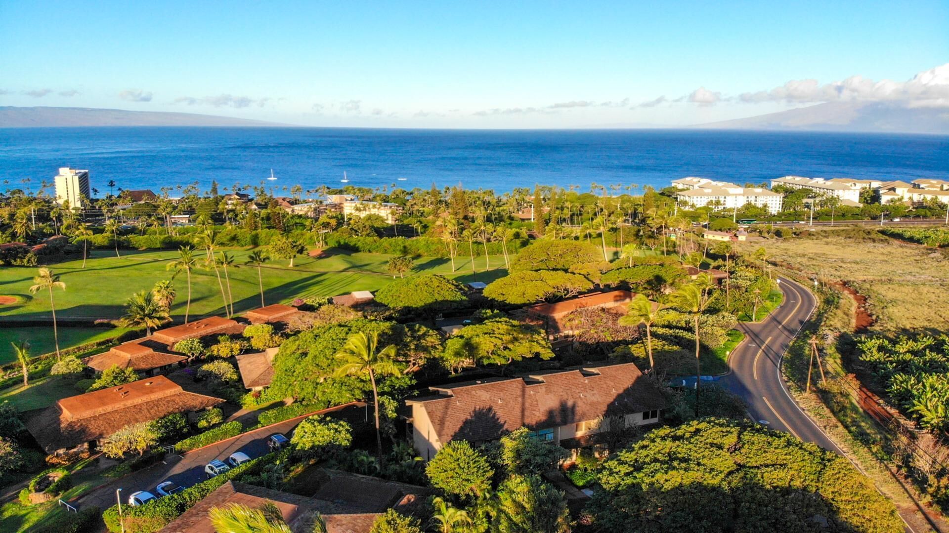 Vista aérea de un complejo turístico costero con un campo de golf, propiedades frente a la playa y una carretera serpenteando por el paisaje.