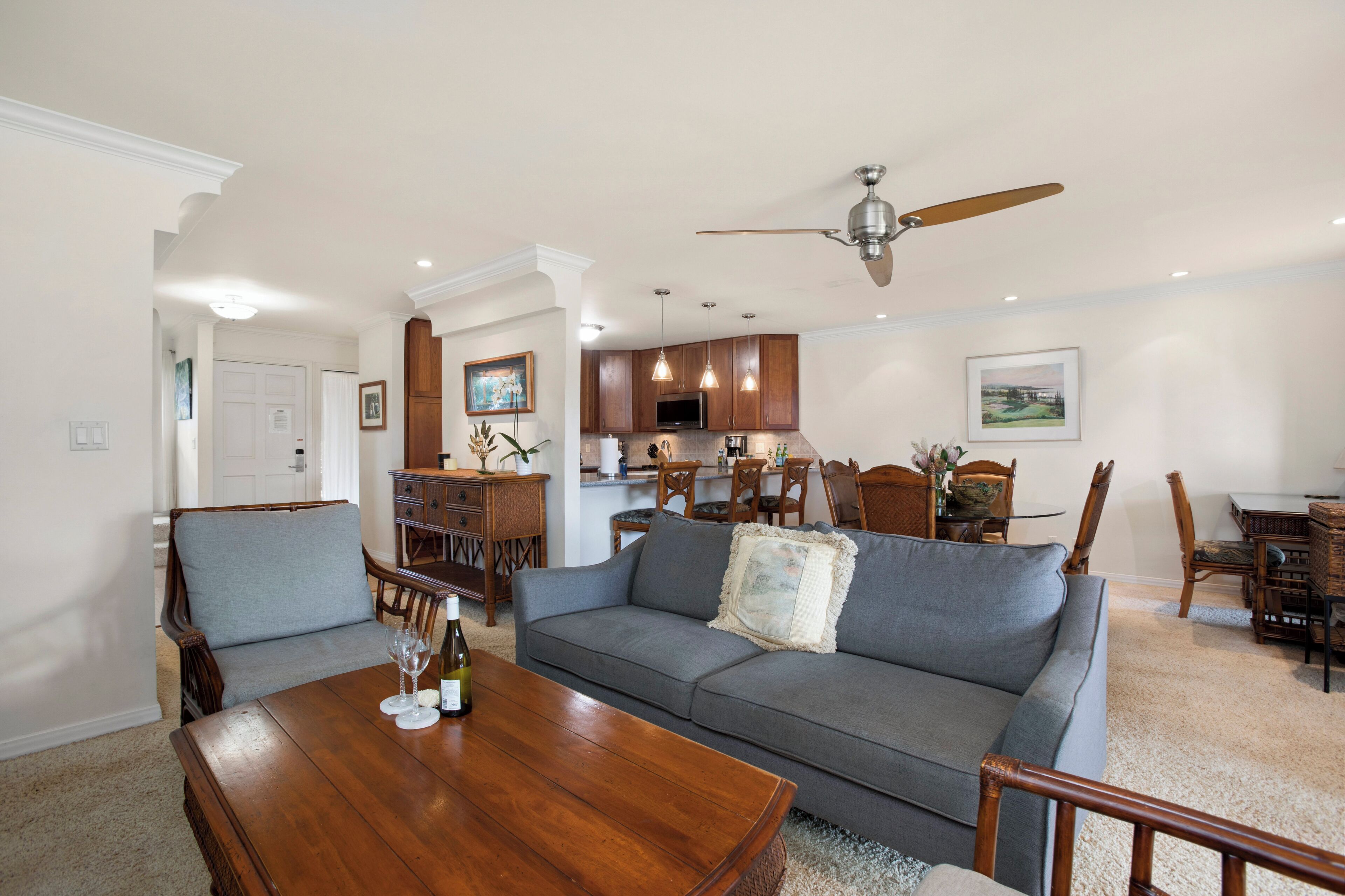 A spacious living room with a wooden coffee table, a gray sofa, and a dining area with wooden chairs and a chandelier.