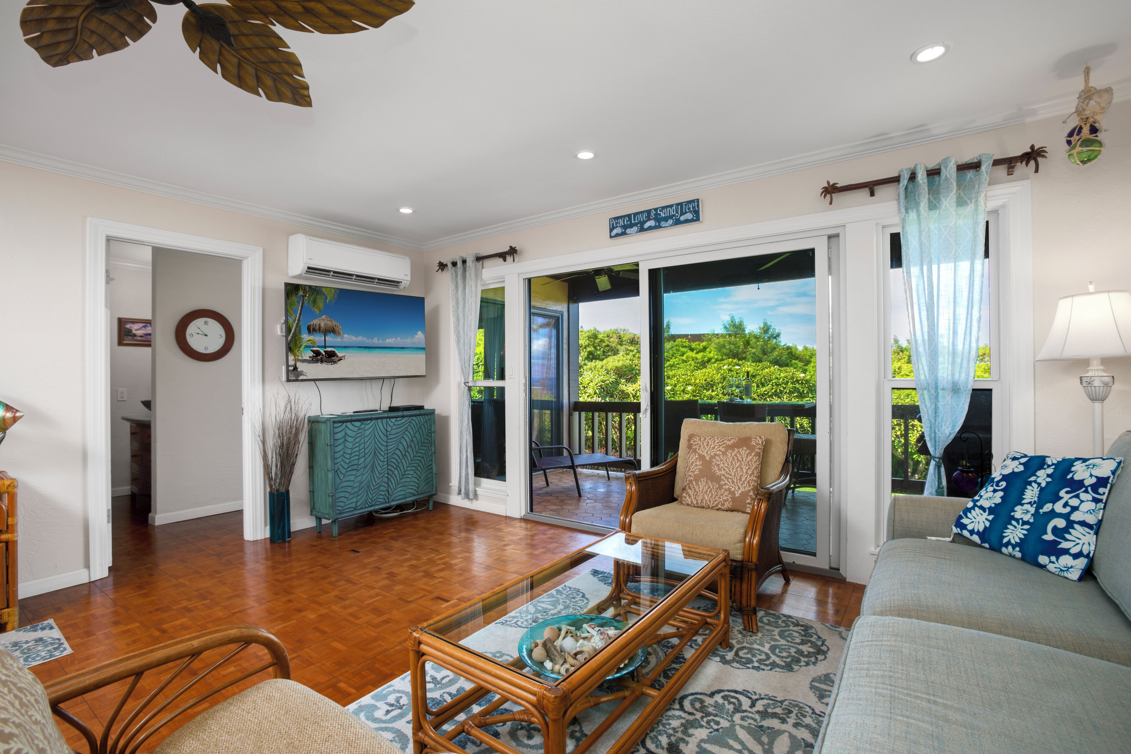 A spacious living room with a glass coffee table, a sofa, and a chair. There is a view of a balcony with a railing and greenery.