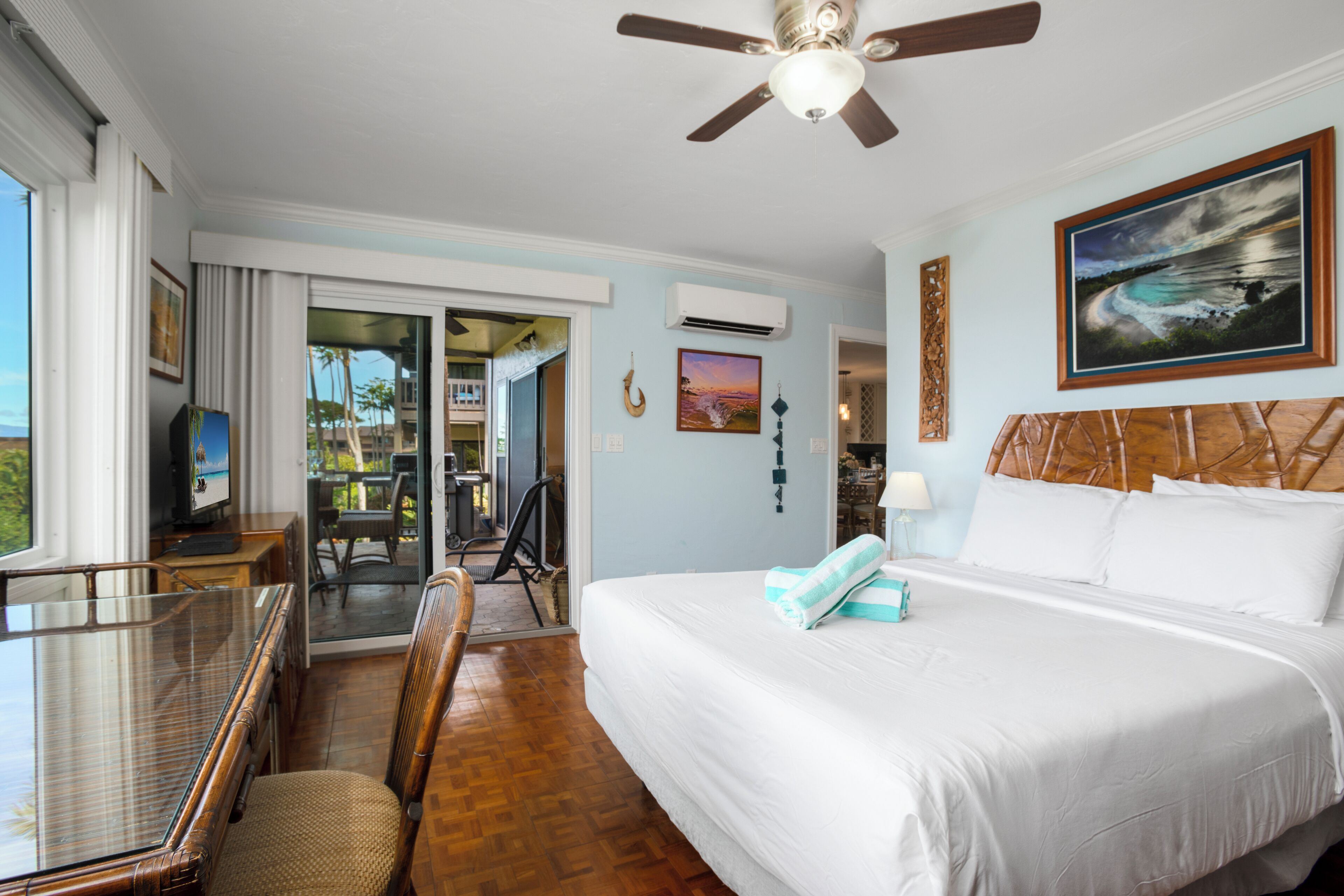 A hotel room with a bed, a desk, a chair, a ceiling fan, and a painting on the wall.