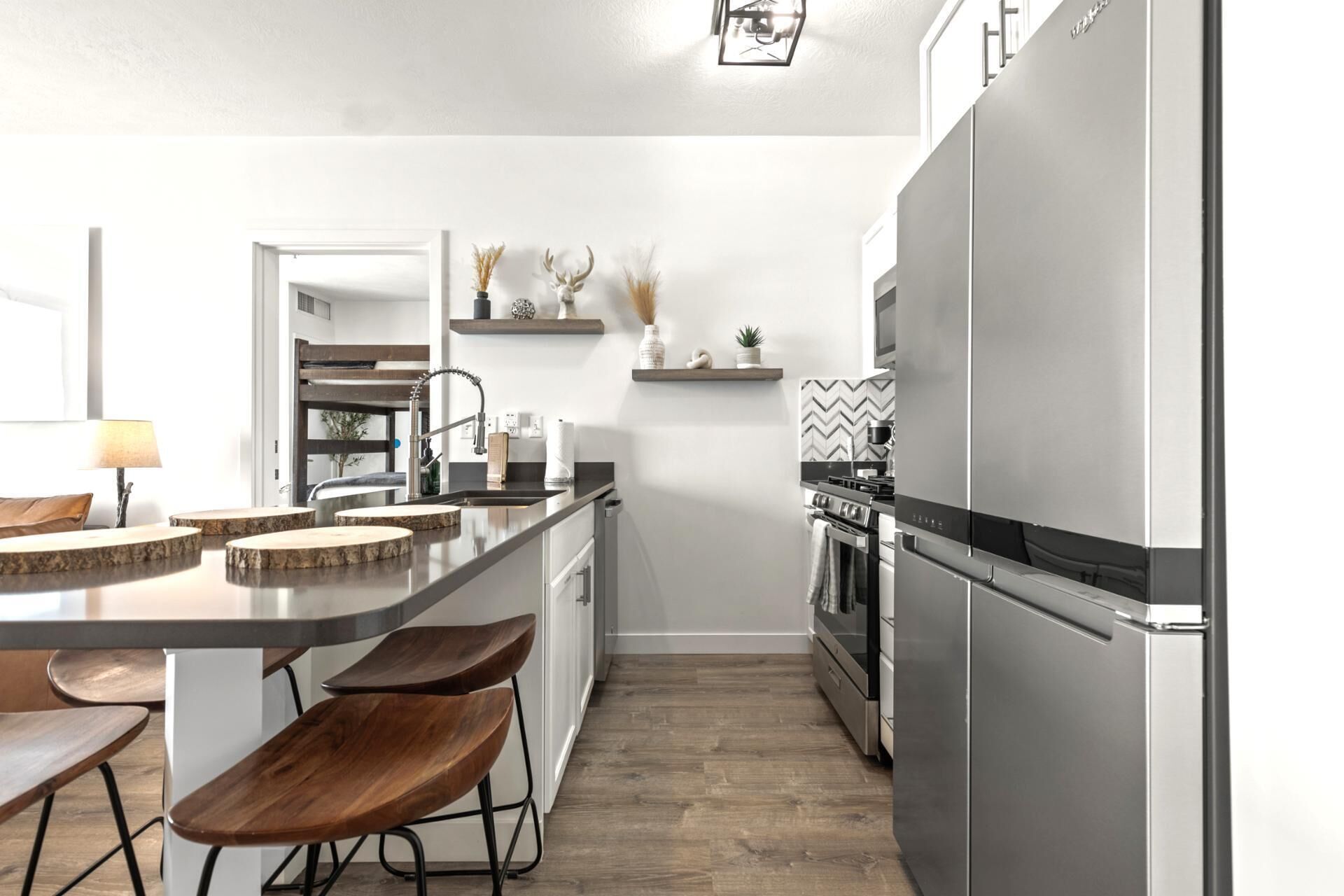 A modern kitchen with a central island, bar stools, a built-in oven, and a stainless steel refrigerator.