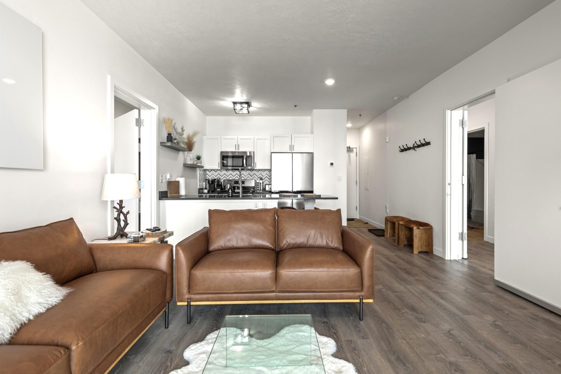 A modern living room with a brown leather sofa, a glass coffee table, and a white fluffy rug.