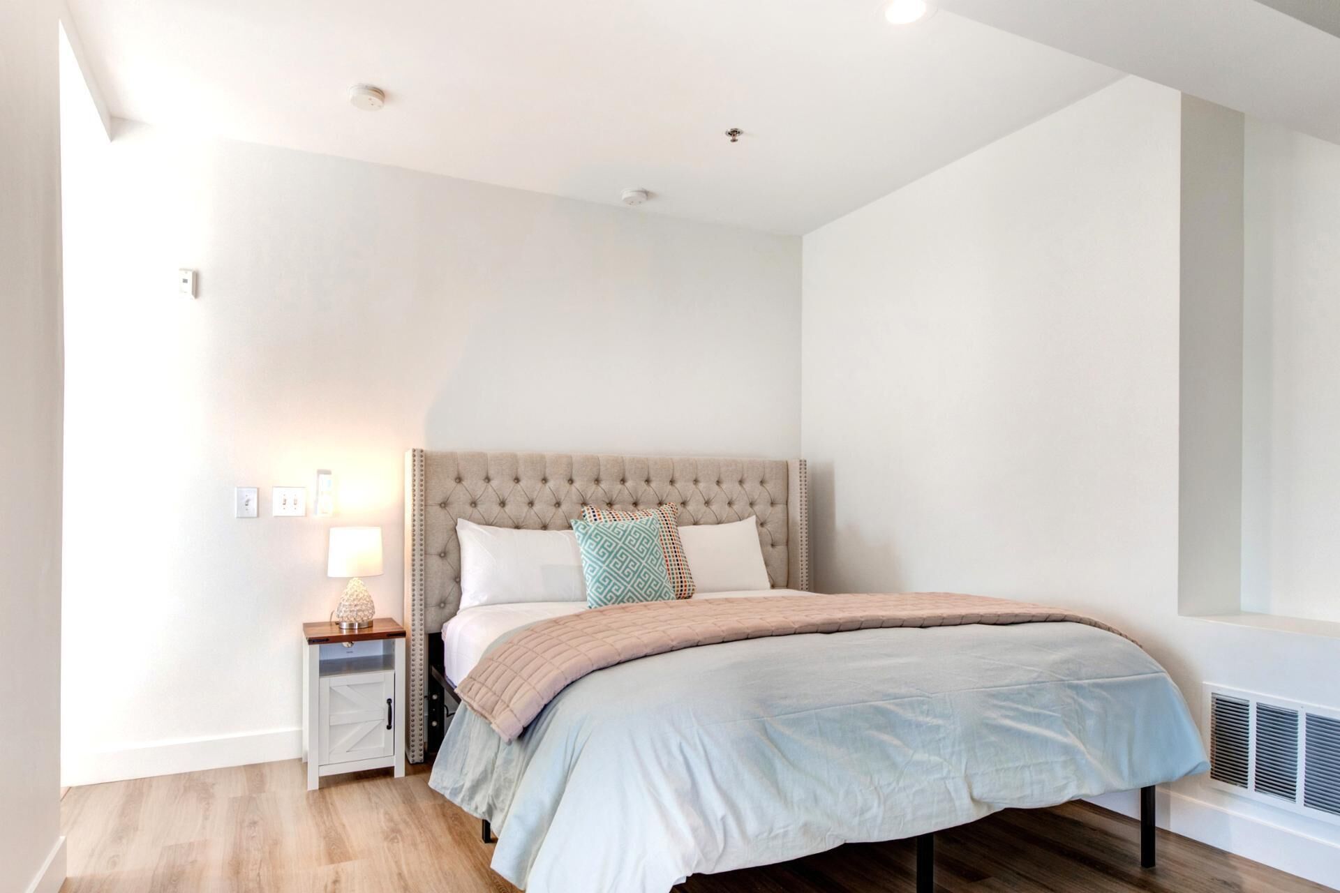 A bedroom with a tufted headboard, a bedside table with a lamp, and a window with a view.