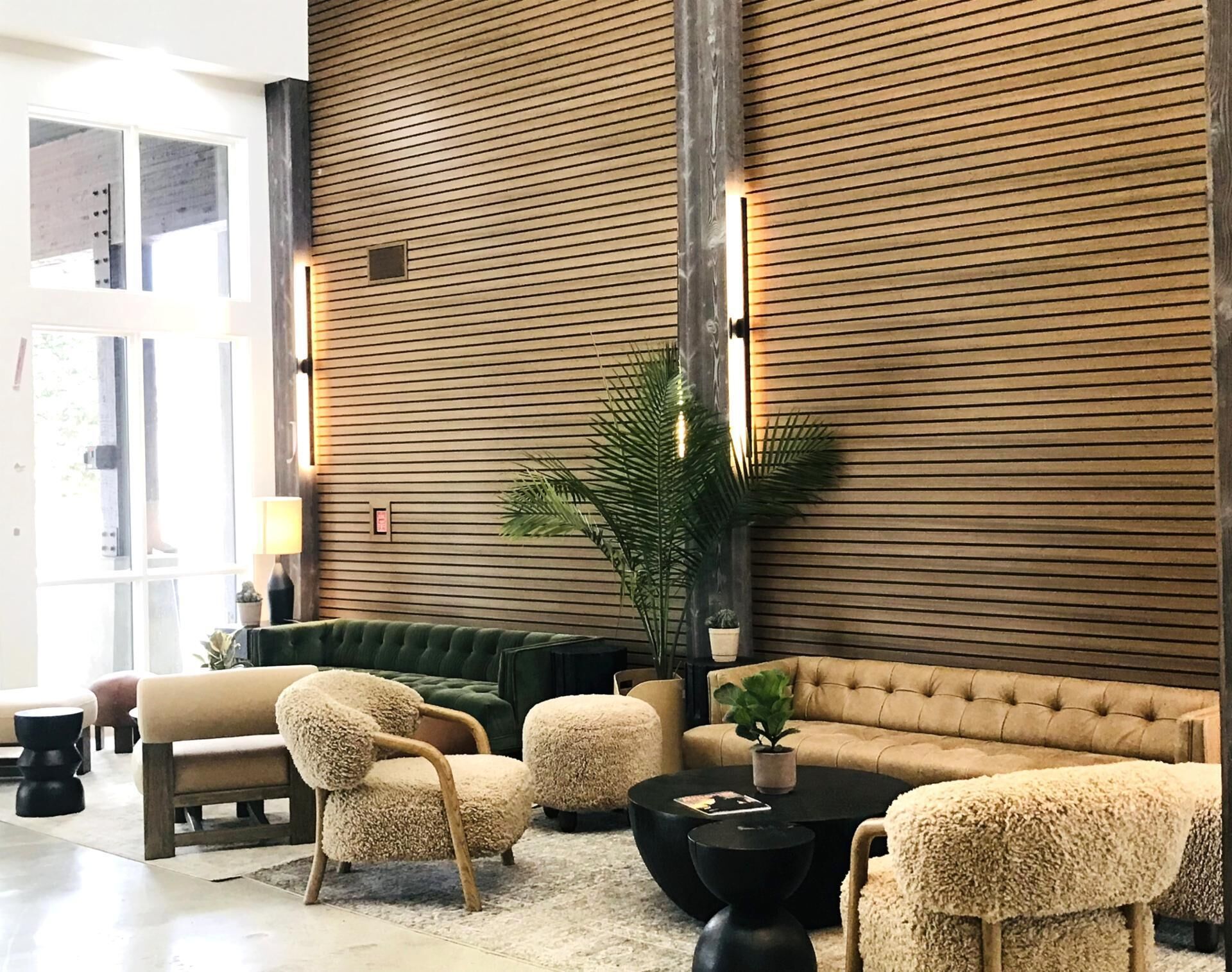 Un vestíbulo moderno con una pared de listones de madera, sofás verdes, sillones mullidos y una planta grande en maceta.