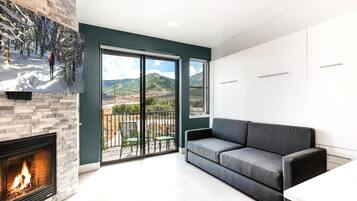 A modern living room with a fireplace, a sofa, and a balcony with a scenic view.