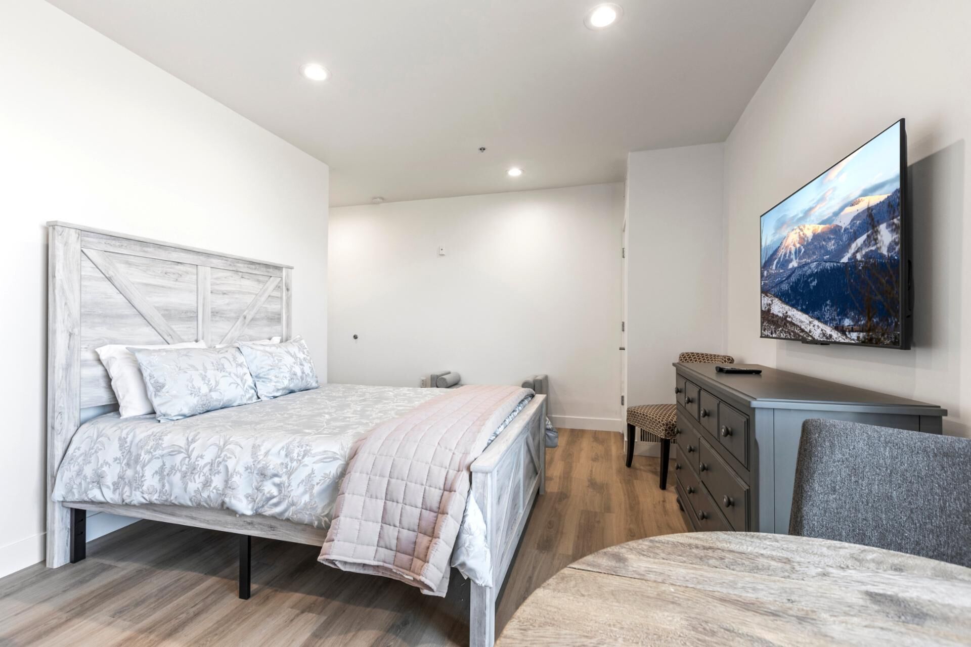 Un dormitorio con una cama, un tocador, una silla y un televisor montado en la pared.