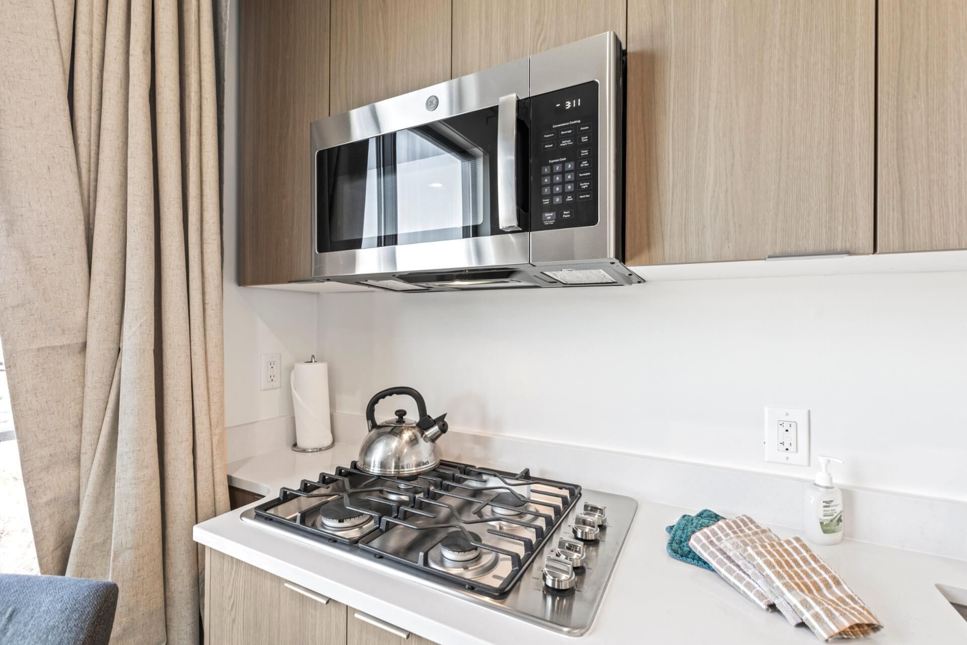 A kitchen with a stainless steel microwave, a gas stove, and a kettle.