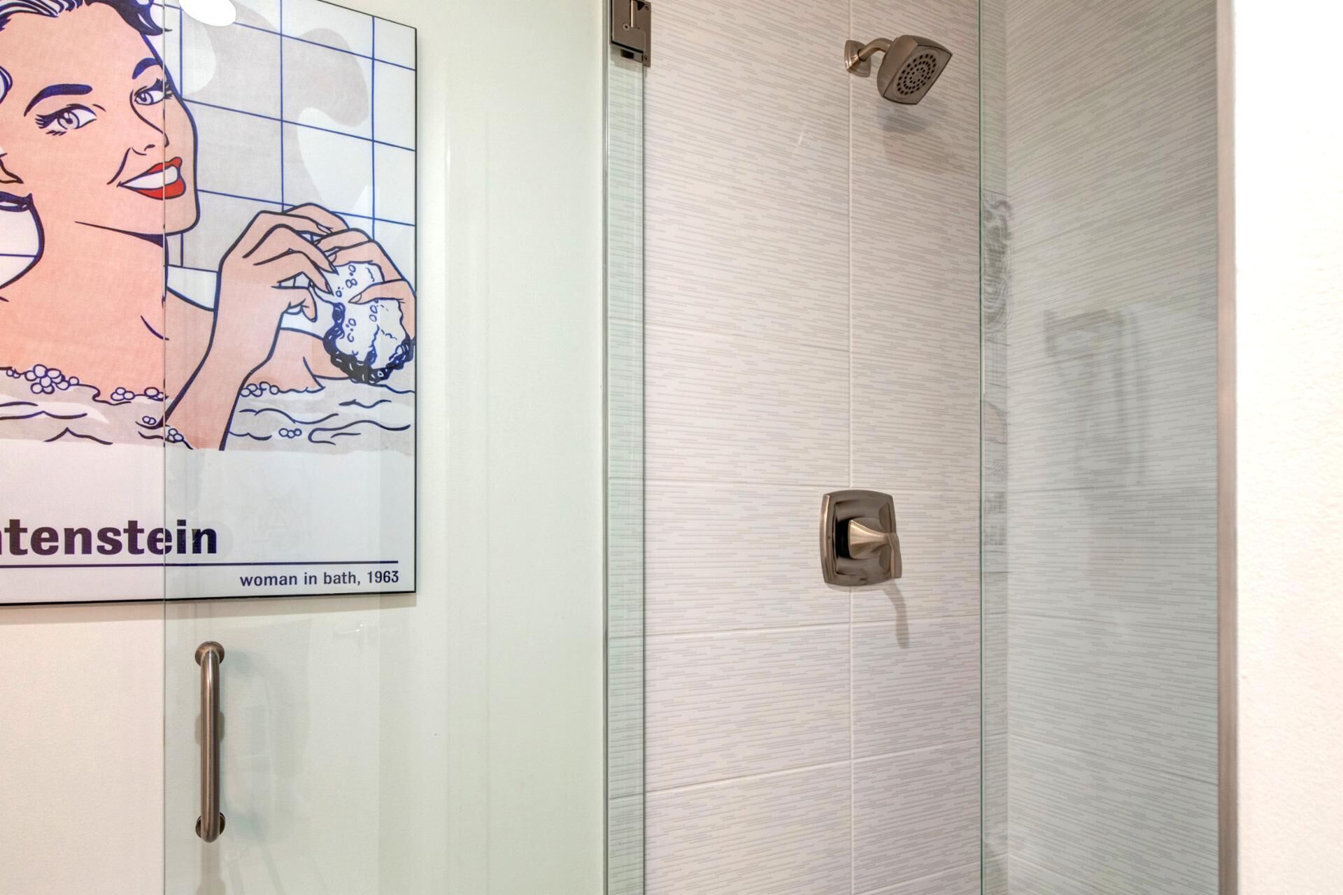 Un baño con ducha, puerta de vidrio y un cartel con una mujer en la bañera.