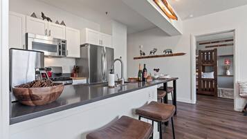 A modern kitchen with white cabinets, stainless steel appliances, and a wooden island with stools.