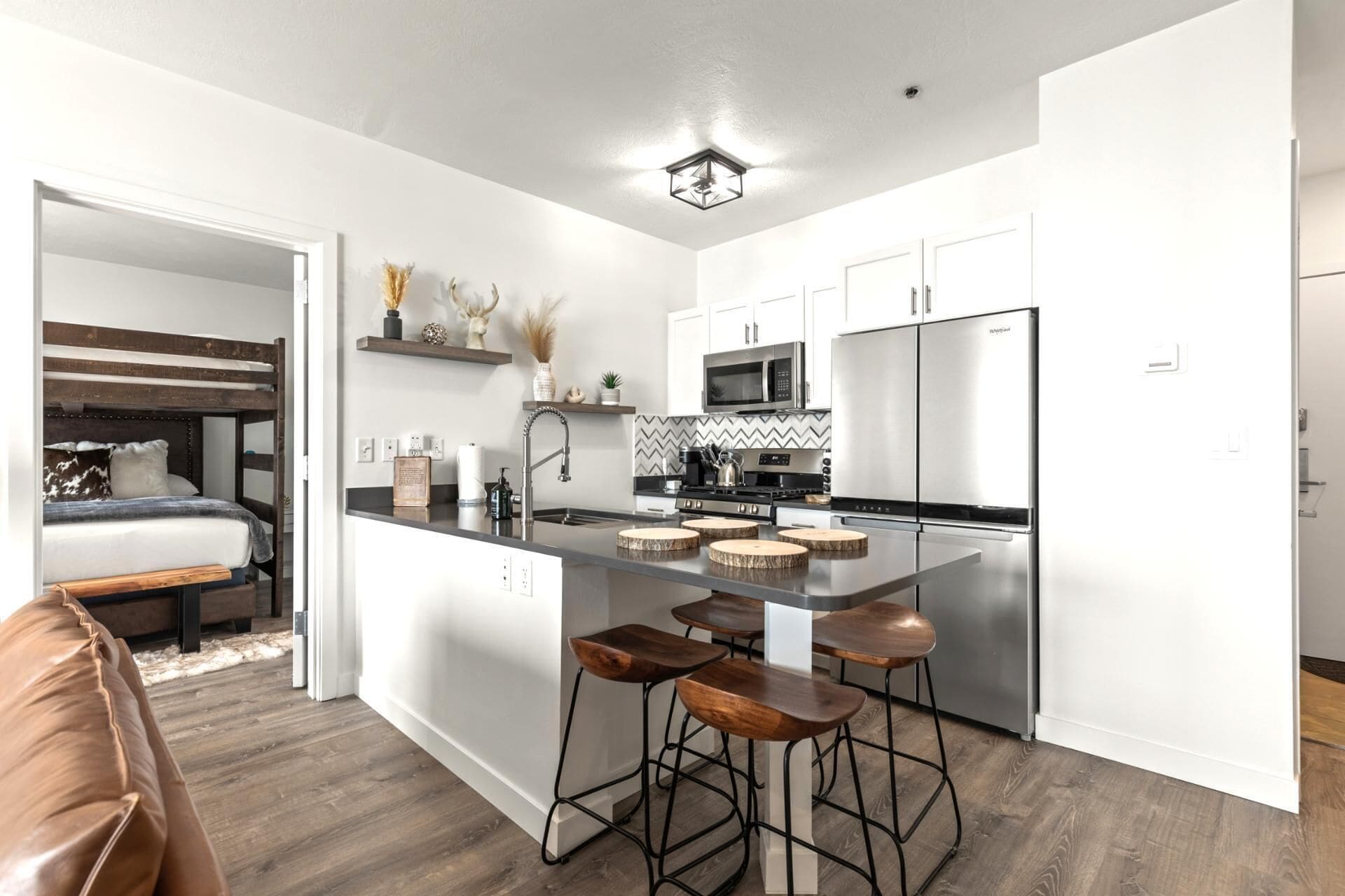 Una cocina moderna con armarios blancos, un refrigerador de acero inoxidable y una isla central con taburetes de bar.