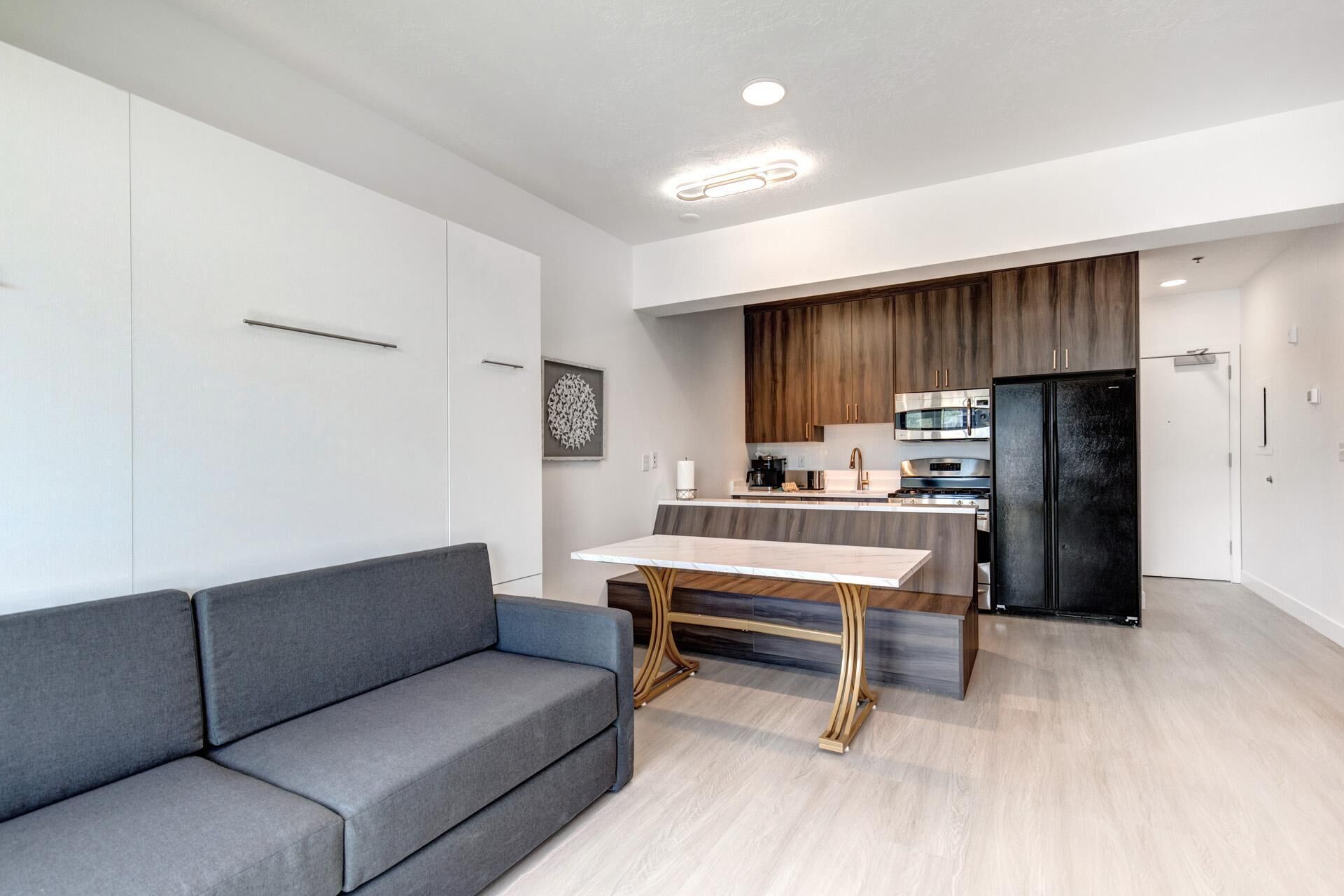 A modern kitchen with a marble countertop, a black refrigerator, and wooden cabinets.
