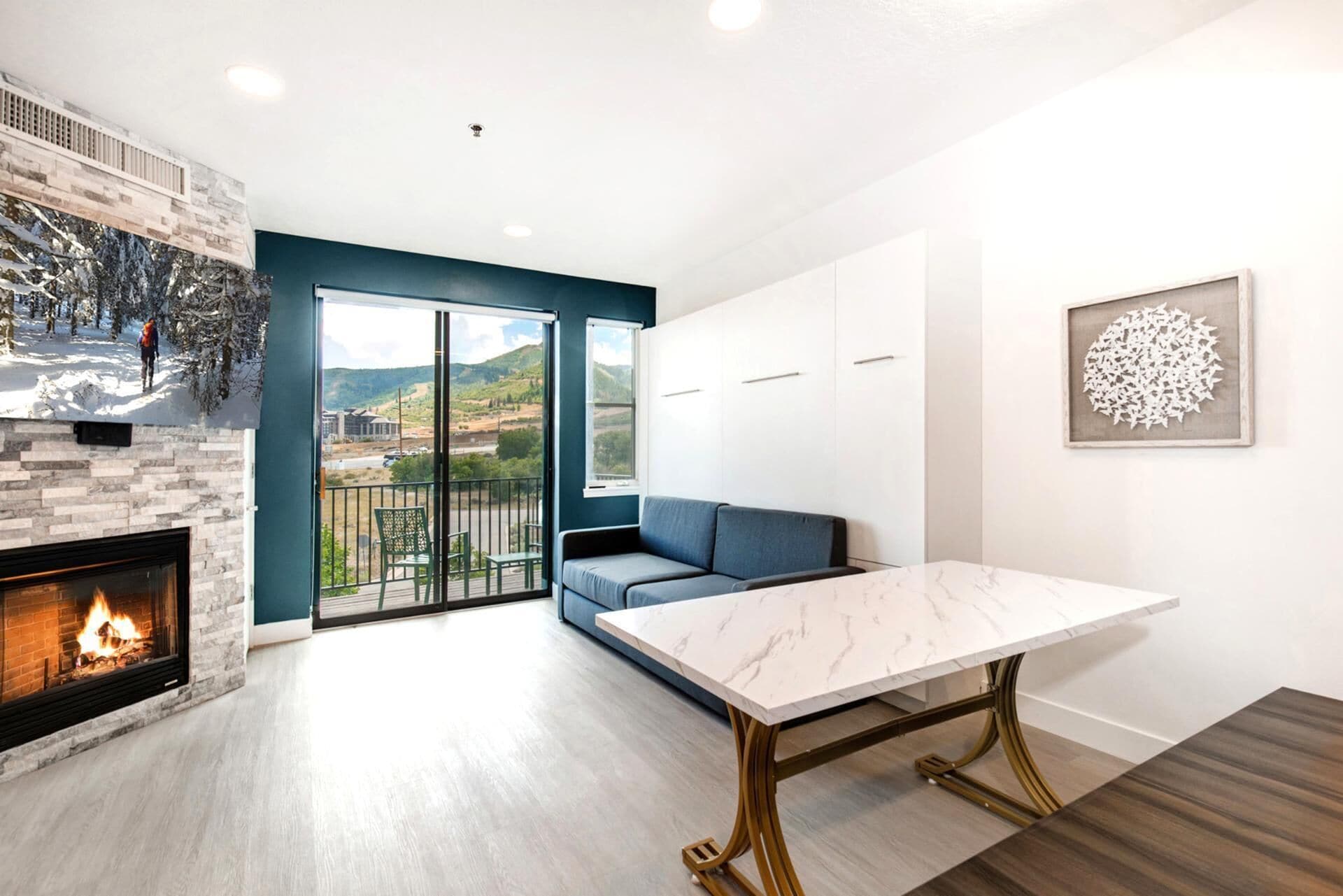 Una sala de estar moderna con chimenea, un ventanal con vistas panorámicas, un sofá azul y una mesa de mármol.