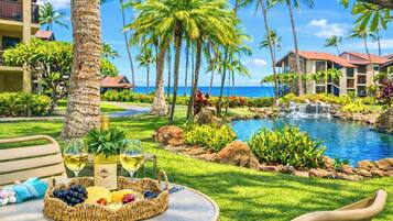 Un entorno de resort tropical con piscina, palmeras y un comedor con mesa dispuesta para dos.