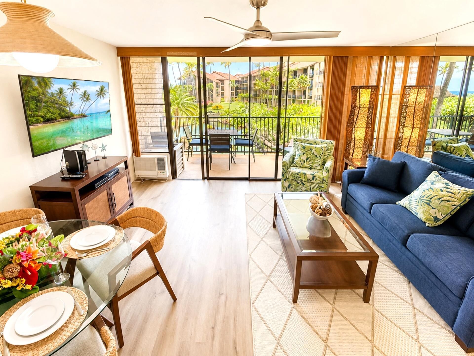 A living room with a TV, dining table, sofa, and a view of a balcony with outdoor furniture.