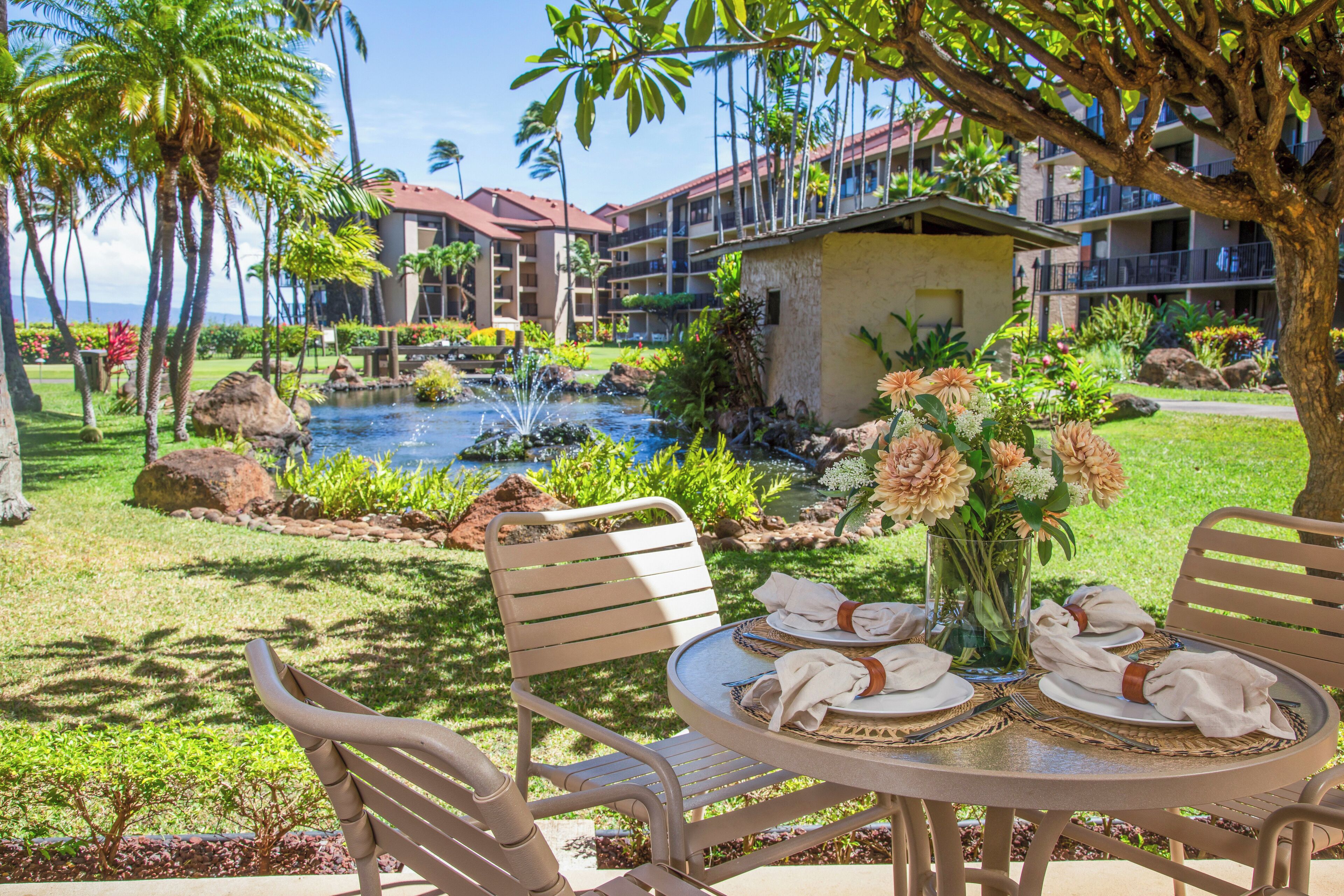 A dining table set outdoors with a view of a pool and hotel buildings in the background.