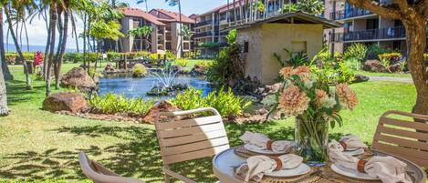 A dining table set outdoors with a view of a pool and hotel buildings in the background.