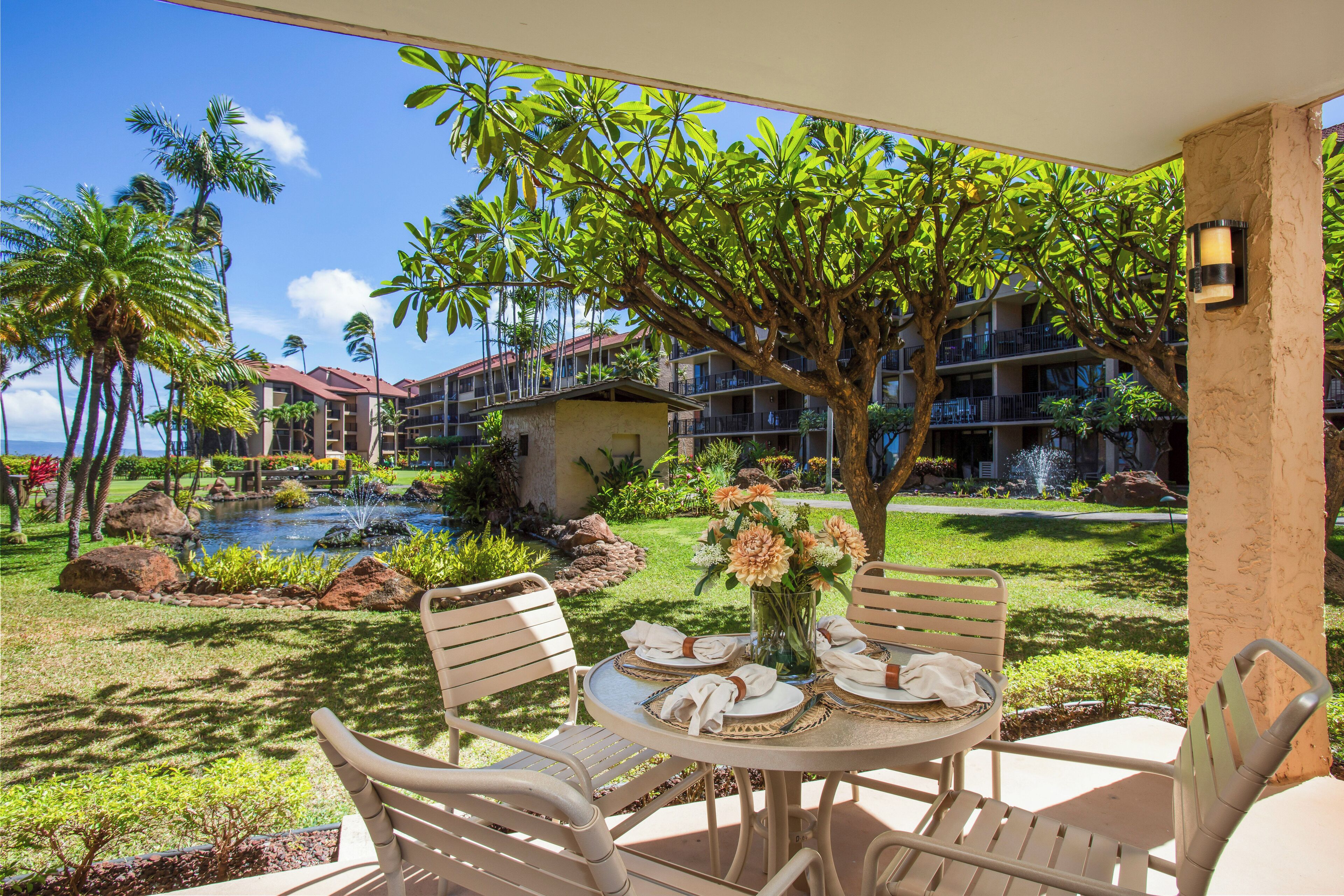 A patio with a table set for dining, surrounded by chairs, palm trees, and a view of hotel buildings.