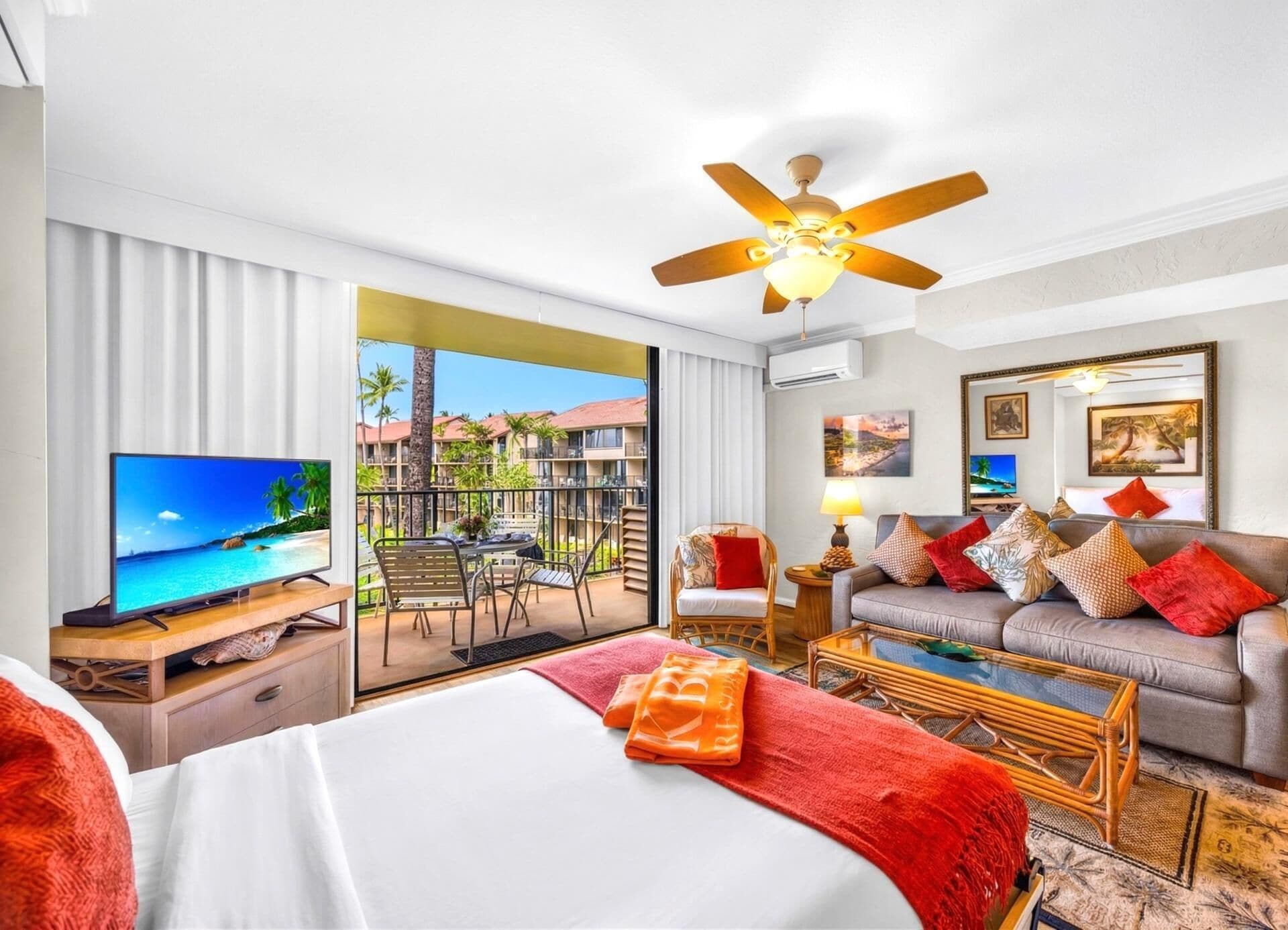 A hotel room with a bed, a TV, a sofa, a coffee table, and a balcony with a view of a resort.