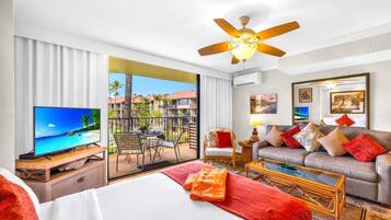 A hotel room with a bed, a TV, a sofa, a coffee table, and a balcony with a view of a resort.