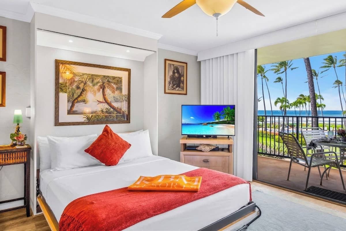 Une chambre d’hôtel équipée d’un lit, d’une télévision, d’un balcon avec vue sur l’océan et d’un ventilateur de plafond.