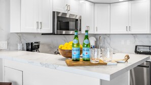 A modern kitchen with white cabinets, a stainless steel microwave, and a marble countertop.