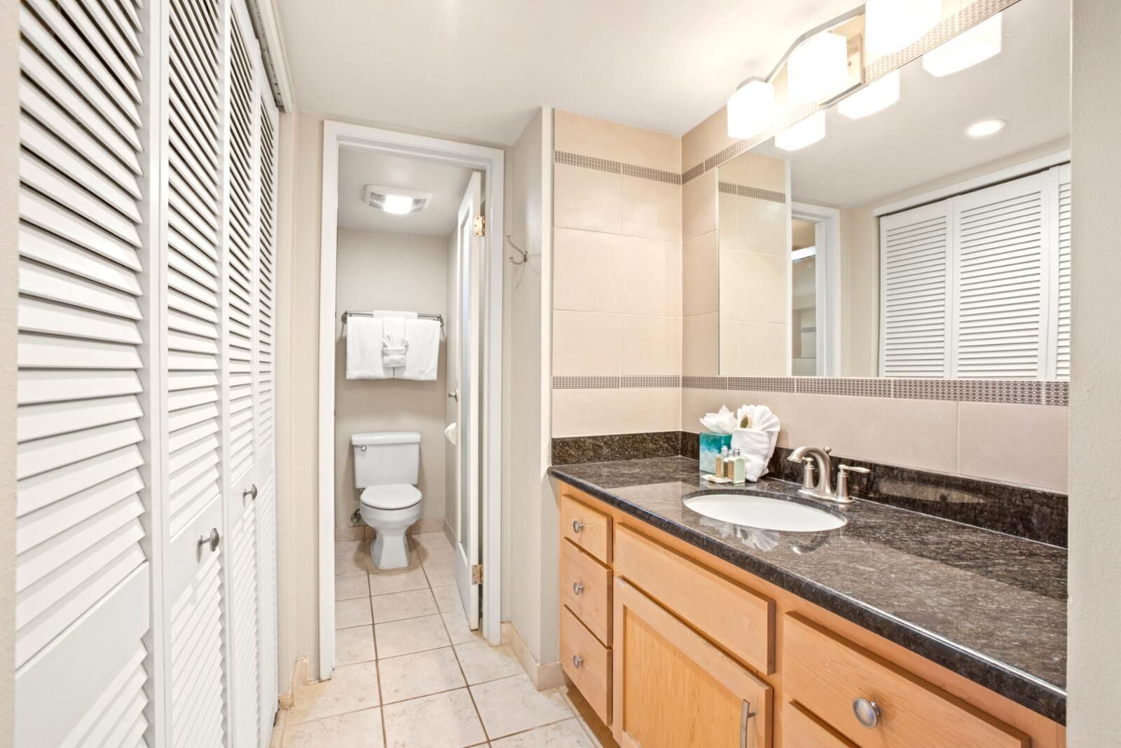 A bathroom with a toilet, sink, vanity, and a mirror.