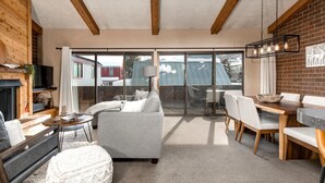 A modern living room with a sofa, dining table, and chairs, a fireplace, and large windows. - Struggler 3 Bedrooms STR-1 by KBM (Park City)