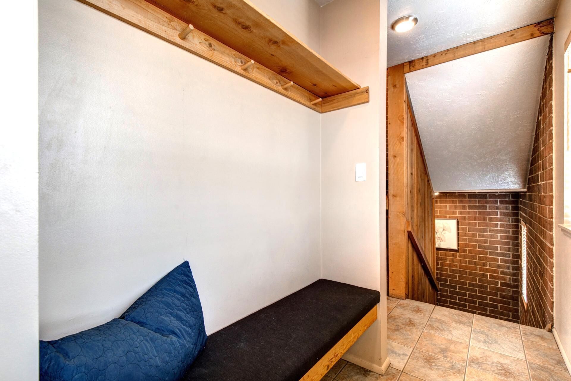 A small, enclosed room with a bench and a blue pillow, a wooden beam ceiling, and a brick wall.