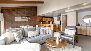 A modern living room with a grey sectional sofa, a wooden coffee table, and a kitchen in the background. - Struggler 3 Bedrooms STR-1 by KBM (Park City)