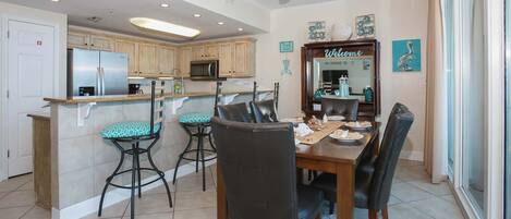 A modern kitchen with a central island, bar stools, and a dining table with chairs.