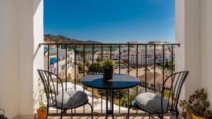 Ein Balkon mit rundem Tisch und zwei Stühlen mit Blick auf eine Stadtlandschaft mit Gebäuden und Bergen.