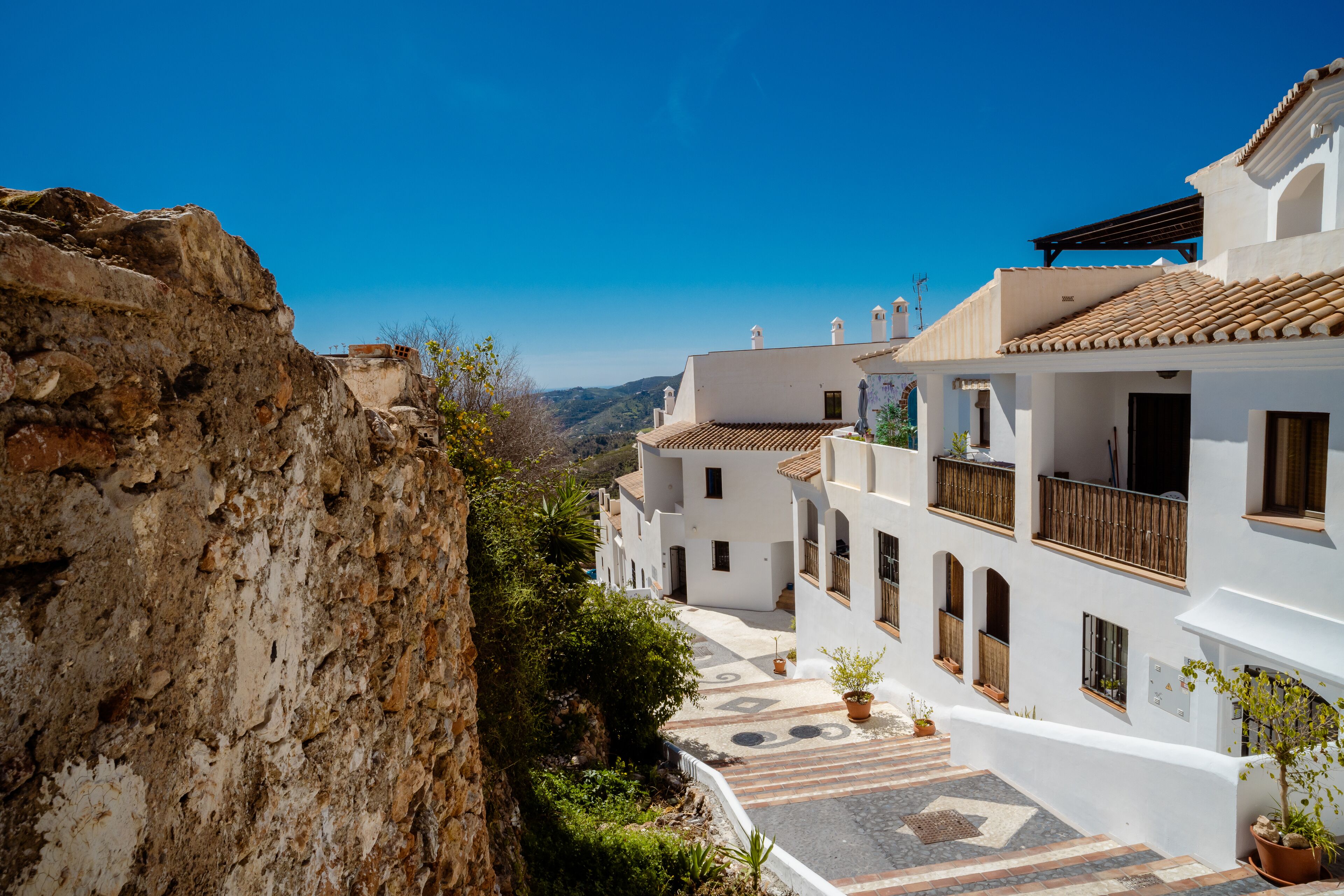 A white building with a tiled roof, a balcony, and a stone wall.