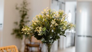 Ein Esstisch mit einer klaren Glasvase mit Blumen, einem Holzstuhl und einer Pendelleuchte.