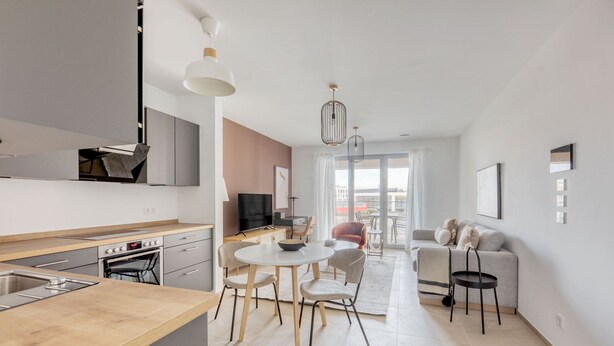 A modern kitchen with a dining area, a sofa, and a view of the outdoors.