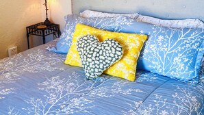 A bed with a blue floral bedspread, a heart-shaped pillow, and a nightstand with a lamp. - Clean, cozy studio nestled in the Grand -Staircase, near the Parks (Boulder)