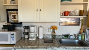 A kitchen with white cabinets, a microwave, a coffee maker, a sink, and various kitchen items on the counter. - Clean, cozy studio nestled in the Grand -Staircase, near the Parks (Boulder)