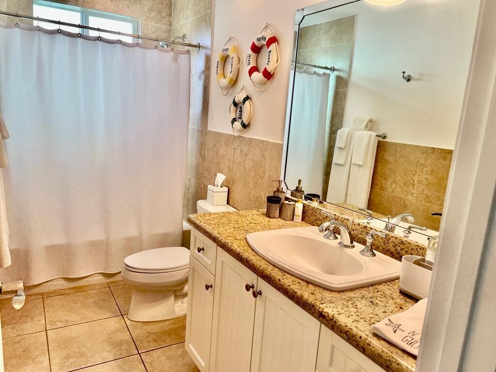 Ein Badezimmer mit Toilette, Waschbecken und Spiegel. Handtücher und Toilettenartikel liegen auf der Ablagefläche.