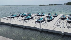 Un ponton de location de jet-skis où plusieurs jet-skis sont alignés sur une jetée qui s’avance dans des eaux calmes.