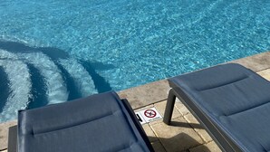 Une piscine d’eau cristalline, bordée de chaises longues, avec un panneau indiquant qu’il est interdit de plonger, et une jetée qui s’avance dans l’océan.