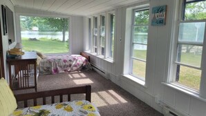 Habitación con cama, una silla y una mesa. Amplias ventanas con vista a un lago.